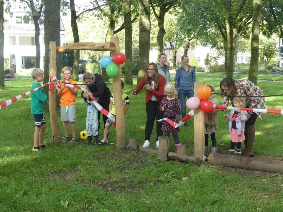 Kinderen en wethouder knippen een lint door dat om de nieuwe houten speeltoestellen is gespannen