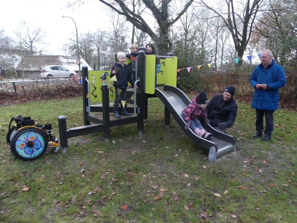 kinderen op de nieuwe glijbaan en wethouder De Graaf kijkt toe