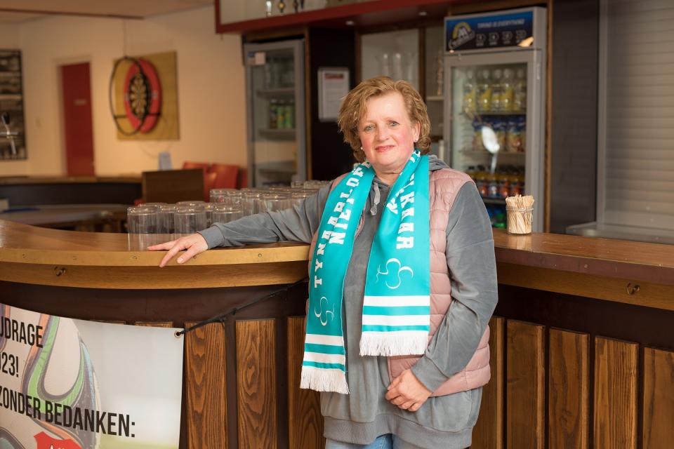 vrouw staat in voetbalkantine met sjaal om waarop staat Tynaatloers laten elkaar niet in de kou staan