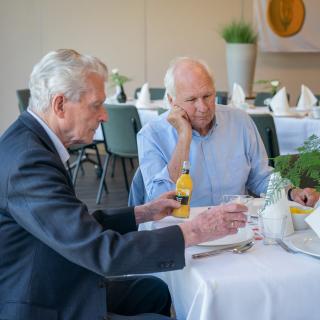 Veteraan schenkt drinken in en zit aan tafel