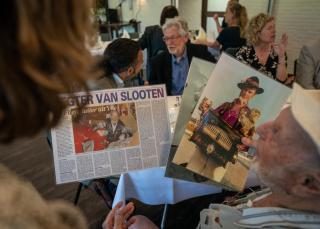 Veteranen lezen een krantje en bekijken foto's van vroeger